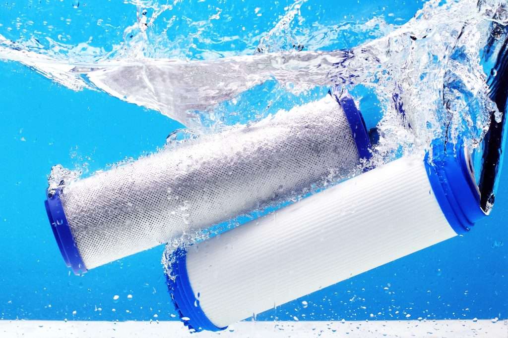 Two white cylindrical water filter cartridges with blue end caps splashing through clear blue water, surrounded by bubbles.