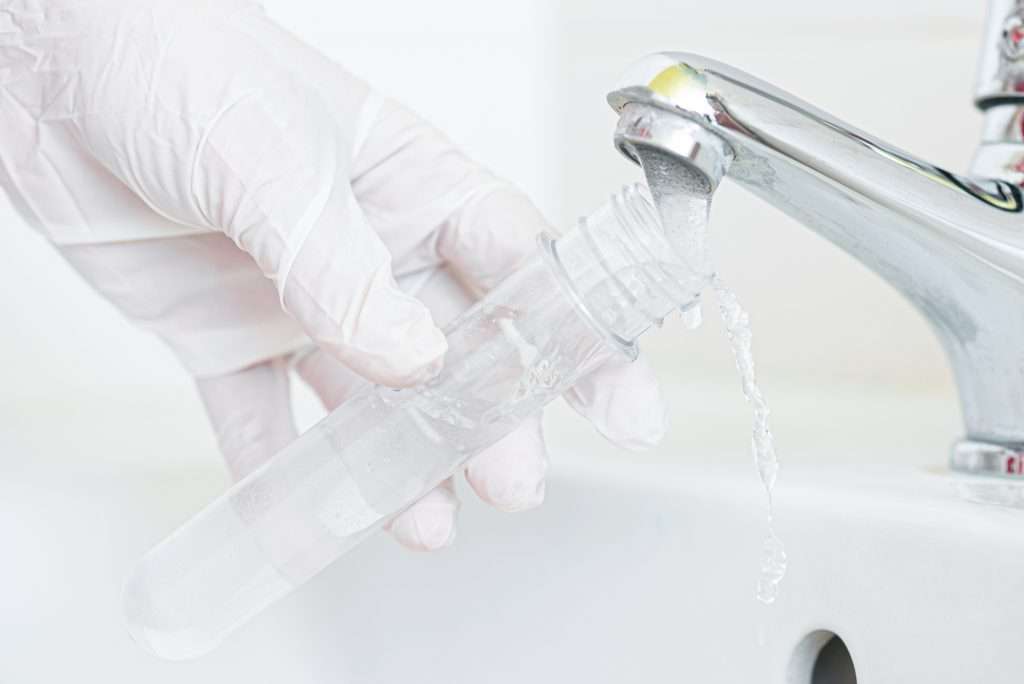 A white-gloved hand filling a test tube with tap water from a home water fixture.