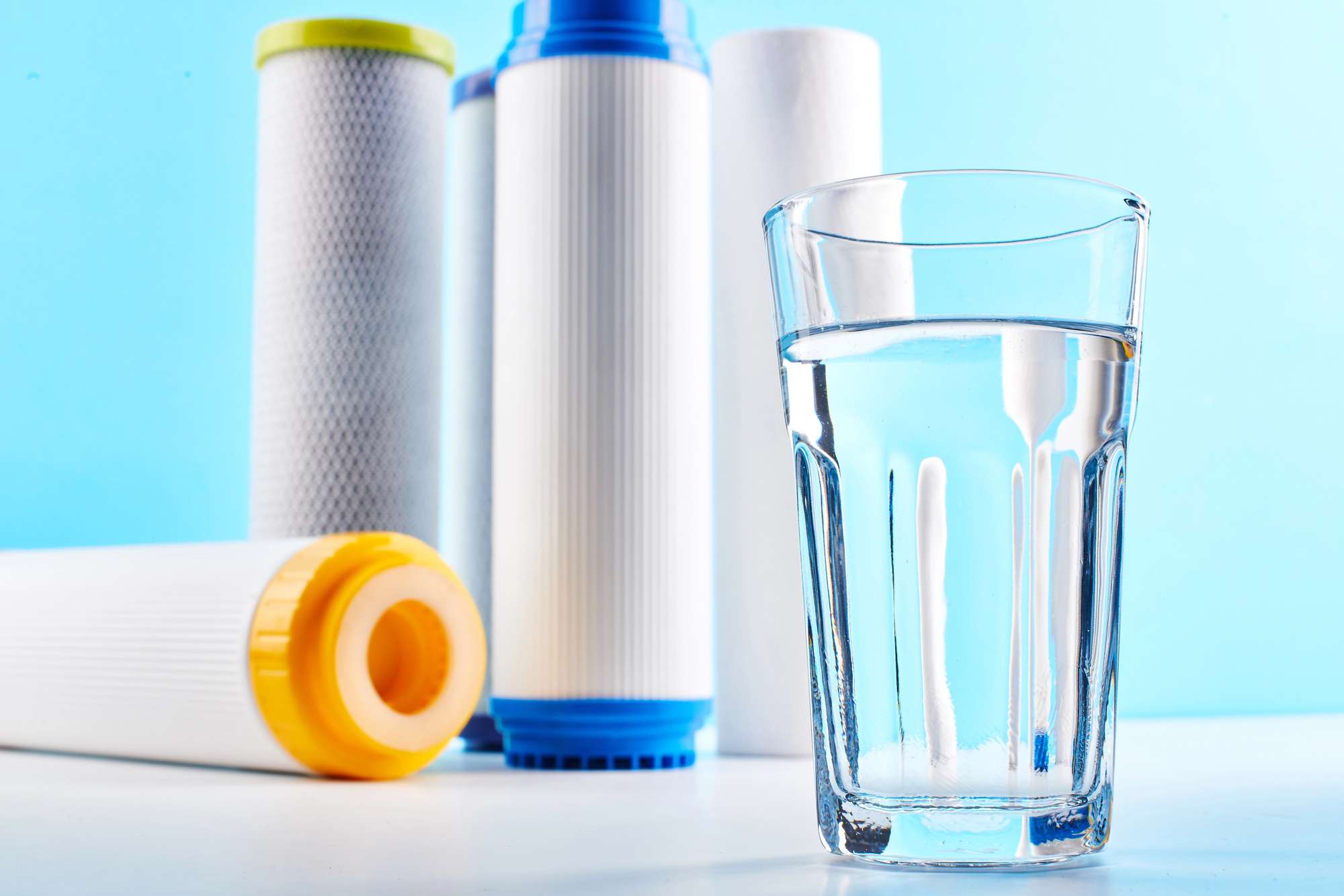 A clear glass of water resting on a white surface with five water filters in the background.