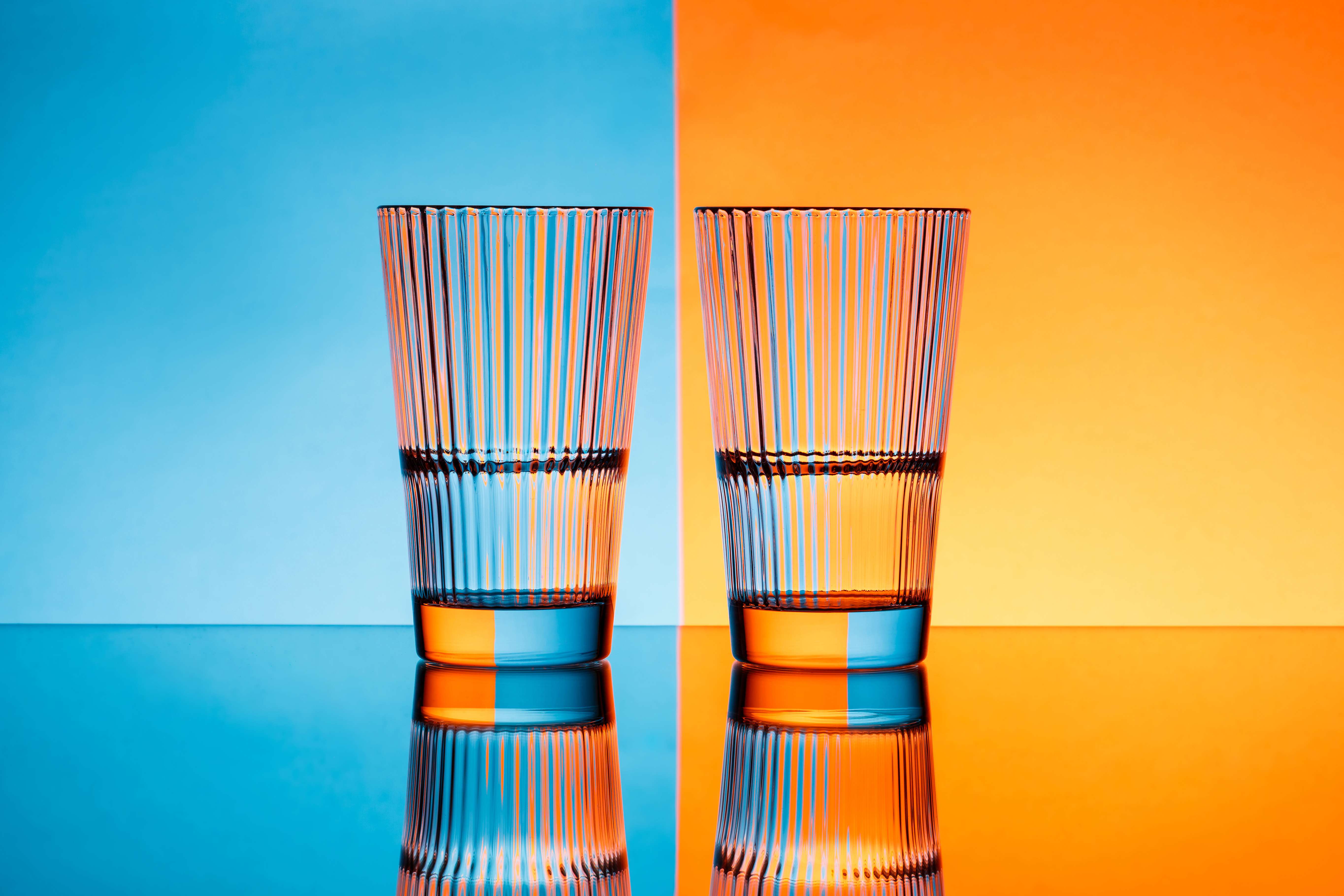 Two glasses with water over a blue and orange background.