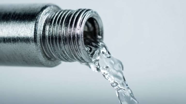 Bright, transparent water streams smoothly from a polished metal pipe with elegant spiral grooves, set against a gentle, luminous backdrop perfect for fluid studies.